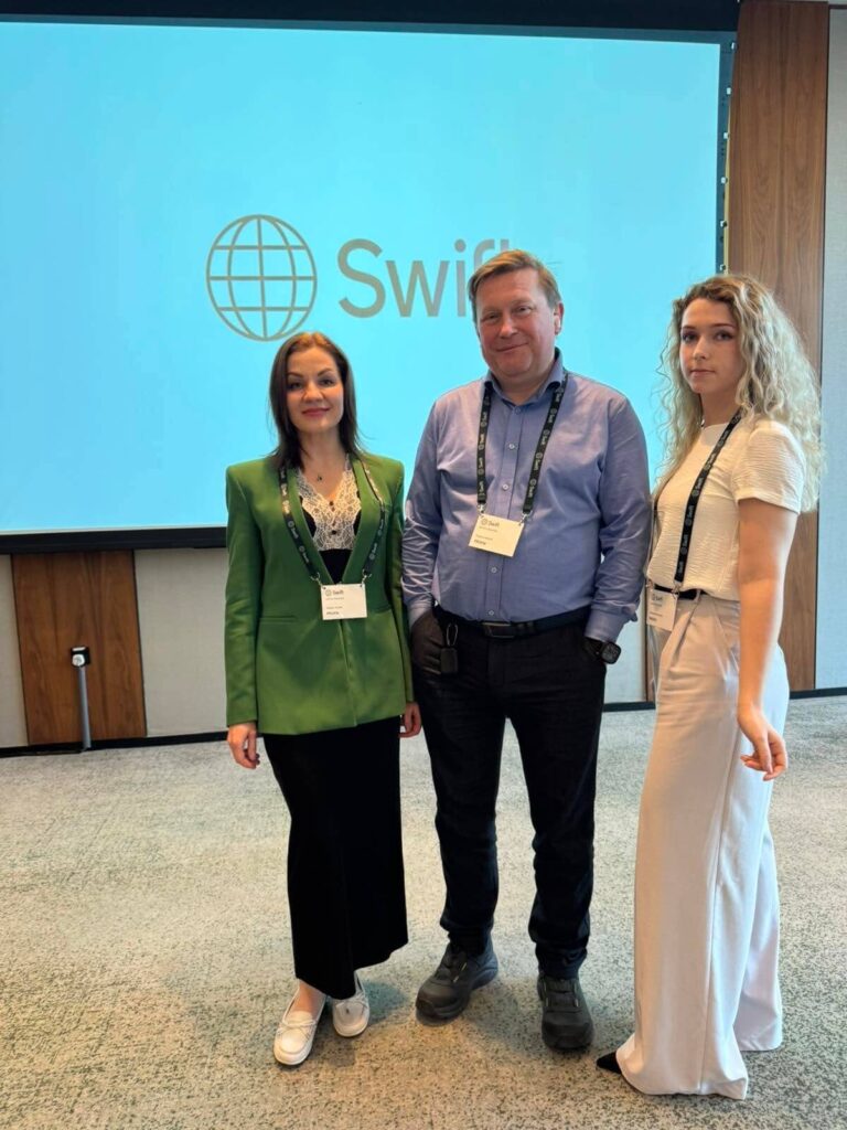Three people from ProFIX Group standing in front of a SWIFT logo at a conference.